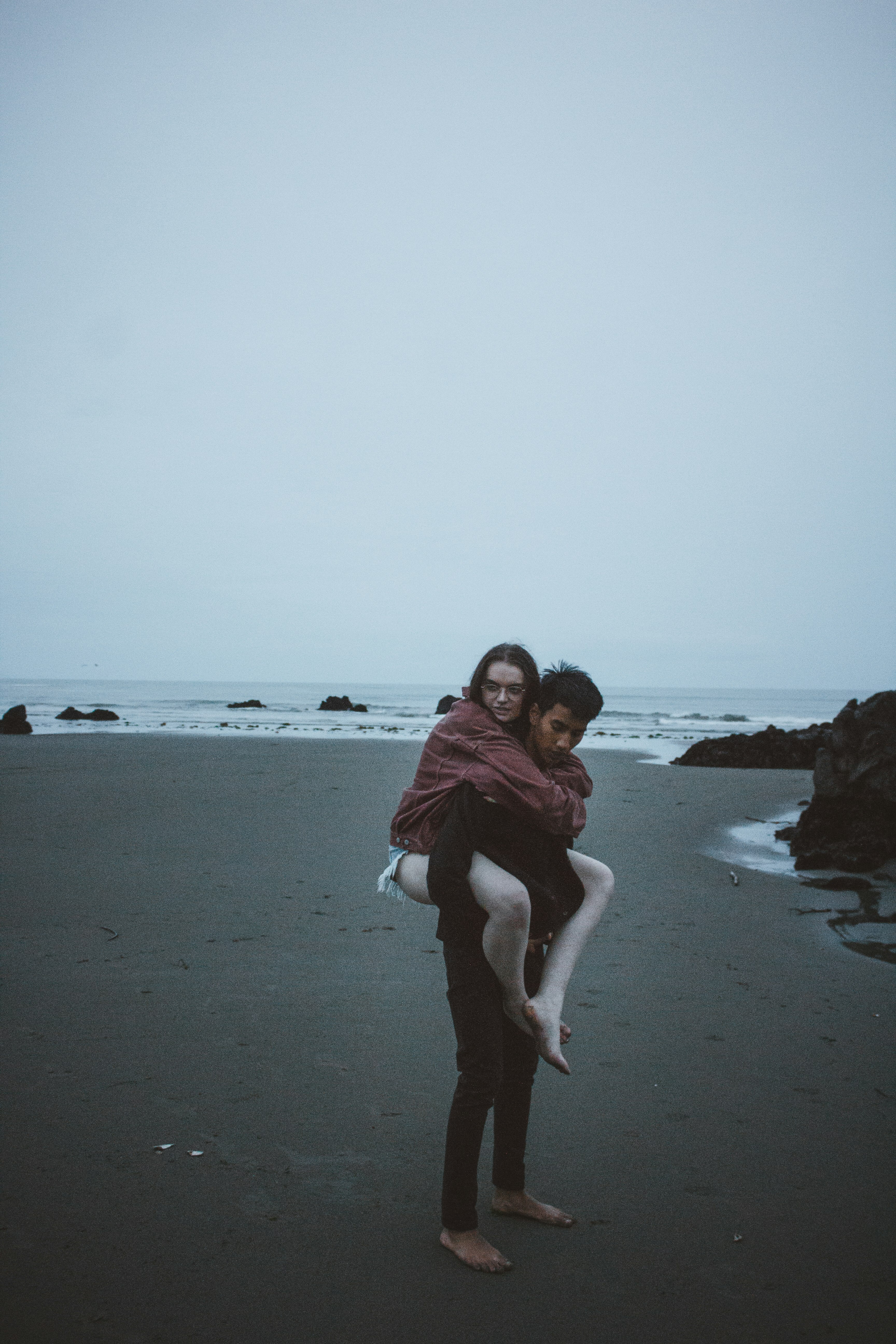 candid photography of man carrying woman at back near seashore